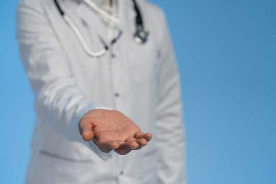 Close-up of male doctor reaching out with open hand in gesture of help or support on blue background, showing healthcare and trust concept.