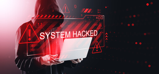 Cybersecurity threat with "System Hacked" warning sign and hooded figure holding laptop on digital background indicating online system breach concept.
