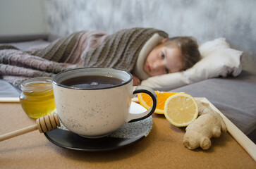 A little girl lies in bed drinking tea with lemon. Concepts of illness, cold, and acute respiratory viral infection.	