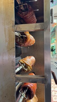 rows of babi guling roasting on metal skewers inside a rotisserie, with golden crispy skin glistening over evenly cooked meat as the pork slowly turns above the heat. the process of roasting porks