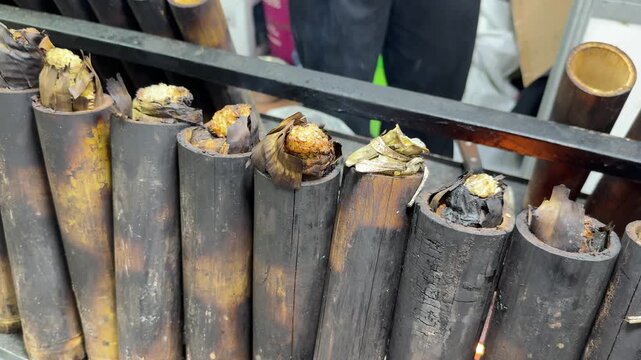 lemang bambu, made from glutinous rice wrapped in banana leaves and cooked inside charred bamboo tubes, slowly roasts over fire. The golden tops show the traditional method of preparing this dish