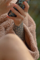 A close-up of a person using a smartphone, wrapped in a soft blanket. The focus on tattooed arm adds a unique touch to this serene moment.