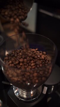 Roasted coffee beans being poured into a grinder hopper with warm caf&eacute; lighting and shallow depth of field. Ideal for specialty coffee branding, caf&eacute; marketing, barista training