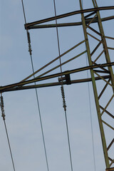Detail of high voltage power lines and tower structure, showcasing electrical infrastructure against a bright blue sky.