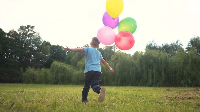 A boy running with colorful balloons. A child is running around with balloons. Colorful grass and colorful grass outside. A young boy dashing with vibrant balloons lifestyle.