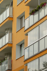 A close-up view of a modern apartment building featuring a vibrant orange facade and balconies adorned with flowers, showcasing contemporary architecture.