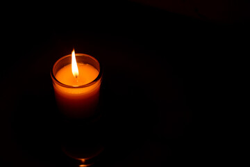 A candle burned on a glass holder in the dark, a symbol of hope.