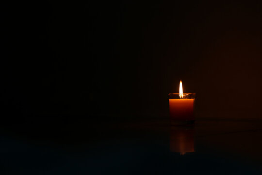 A candle burned on a glass holder in the dark, a symbol of hope.
