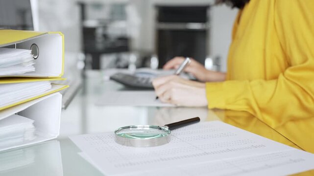 Woman accountant in yellow blouse calculating finances and analyzing data in office, performing tax document audit. Audit and taxes in business