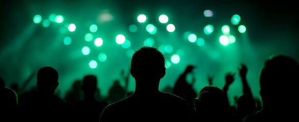 Green concert crowd illuminated by lights with energetic silhouettes celebrating together.