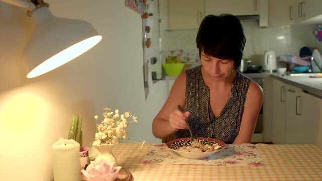caucasian woman testing homemade dish at kitchen table stirring spoon tasting and adjusting seasoning evening warmth