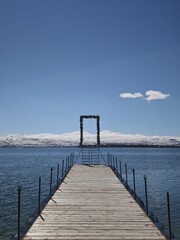 Obraz premium a wooden pier on a calm mountain lake or sea, set against snow-capped peaks and a clear sky.