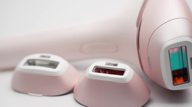 A pink IPL hair removal system with three attachments slowly rotates on a white background. Video showcases the main handset and interchangeable heads.