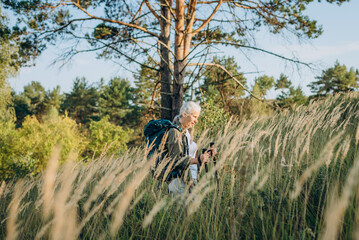Senior woman walks through tall grass field while backpack frames profile