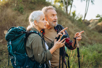 Senior woman holds smartphone while mature man pointing ahead