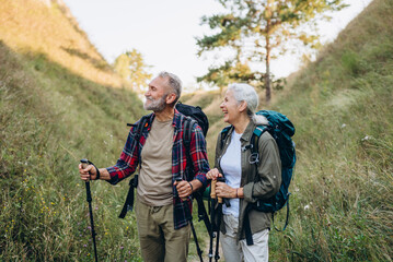 Senior couple stands in grassy ravine while backpacks rest on shoulders