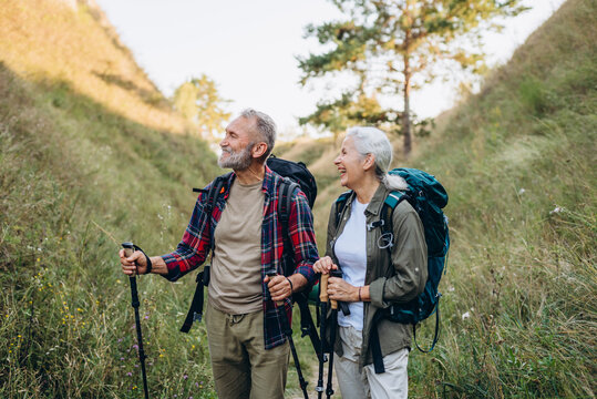 Senior couple stands in grassy ravine while backpacks rest on shoulders
