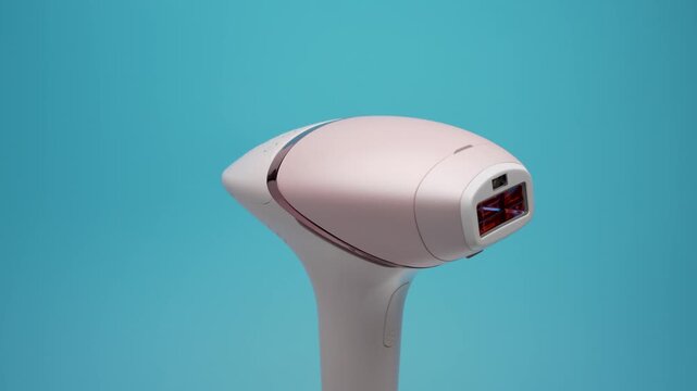 A pink IPL hair removal device slowly rotates in front of a turquoise backdrop. The side profile highlights the slim handle and compact flash window.