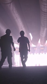 silhouette of many construction workers walking out from a large tunnel