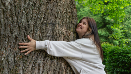 Joyful Young Woman Happily Hugging a Large Tree Trunk, Expressing Love and Connection with Nature in a Green Park.