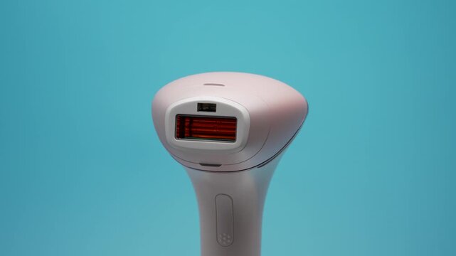 A pink IPL hair removal device slowly rotates against a turquoise background. Front view shows the rectangular flash window and sensor area.
