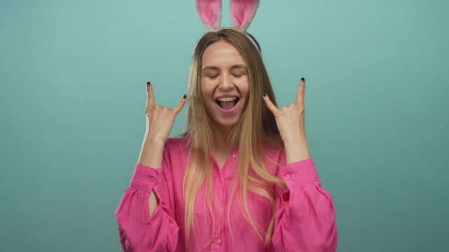 Young woman with easter bunny ears posing joyfully against an isolated green wall background, expressing happiness and fun with her hands and smile.
