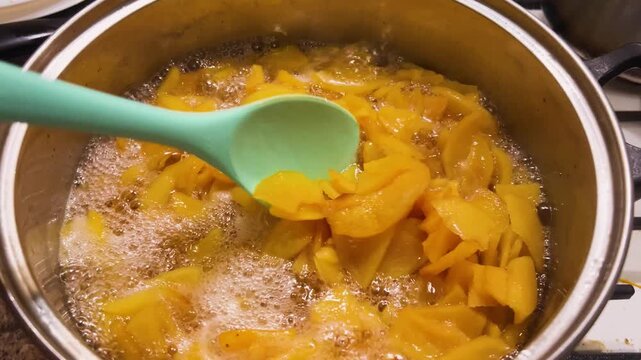 Quince jam is boiling in a large saucepan. Stirring the jam with a silicone spatula.