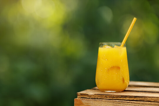 glass of cold orange juice or summer cocktail with ice and straw