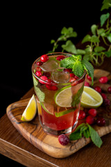 A tall glass filled with a vibrant berry mint drink showcases ice, fresh mint leaves, and lime slices. The wooden board beneath adds a rustic touch, enhancing the drink's colorful appeal