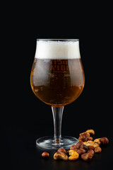 A tall glass of golden beer, topped with frothy foam, stands proudly next to a small pile of roasted nuts. This setup invites cozy gatherings and festive celebrations
