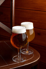 Two elegantly shaped glasses filled with craft beer rest on a wooden table in a cozy setting. The warm lighting enhances the inviting atmosphere, perfect for socializing and exploration