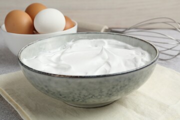 Beating whites in bowl, eggs and whisk on grey textured table, closeup