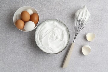 Beating whites in bowl, eggs, eggshell and whisk on grey textured table, flat lay