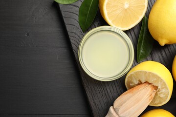 Fresh lemon juice, fruits and squeezer on black wooden table, flat lay. Space for text