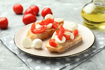 Tasty bruschettas with mozzarella cheese and tomatoes on grey textured table, closeup