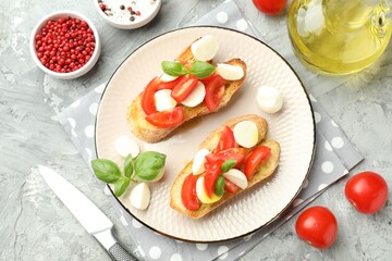 Tasty bruschettas with mozzarella cheese, tomatoes, basil and spices on grey textured table, flat lay