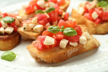 Tasty bruschettas with mozzarella cheese, tomatoes and basil on white plate, closeup