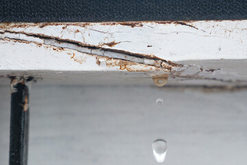 Water leak dripping from cracked window frame in a house