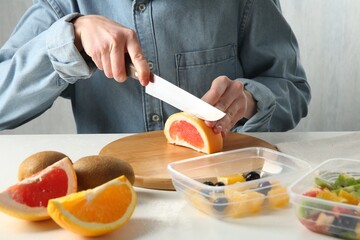 Making fruit salad. Woman cutting grapefruit at white table, closeup
