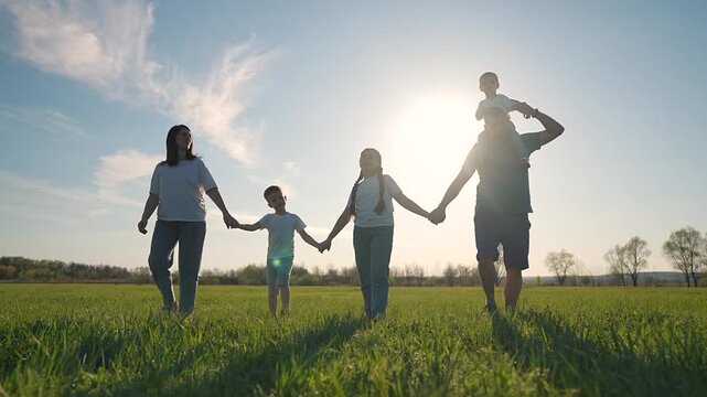 Parents holding hands daughter. Group walking forward on grass. Father walks near children. Holding hands across green field. Walking daughter. Family line walking. Father, walking, holding repeated.
