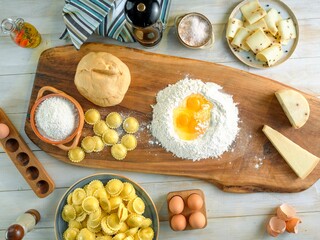 On a rustic wooden table, fresh ingredients are laid out for making pasta. Flour, eggs, cheese, and...