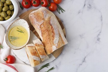 Tasty baguette served with oil, tomatoes, rosemary and olives on white marble table, flat lay. Space for text
