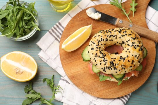Delicious bagel with salmon, cream cheese, cucumber, arugula and lemon on light blue wooden table, flat lay - Powered by Adobe