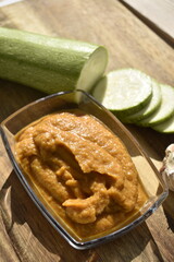 Zucchini caviar in glass bowl with sliced fresh zucchini and garlic on wooden background, top view