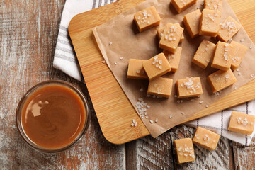 Tasty candies with salt and caramel sauce on color wooden table, flat lay