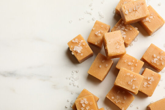 Tasty caramel candies with salt on light marble table, flat lay. Space for text