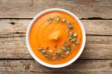 Tasty pumpkin cream soup with seeds served on wooden table, top view