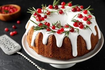 Tasty Christmas cake with icing, cranberries and rosemary on black table, closeup