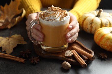 Woman holding tasty pumpkin latte with whipped cream at grey table, closeup