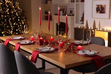 Stylish Christmas table setting with plates, glasses and burning candles in festive decorated room, closeup. Bokeh effect